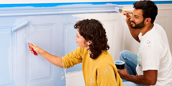 Un couple peint un mur avec du ruban de masquage Scotch®.
