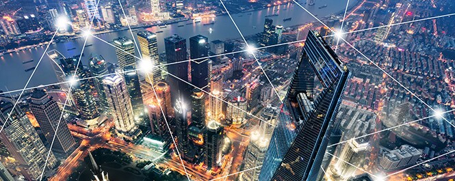 Vue d’une ligne d’horizon urbaine, survolée d’un maillage géométrique de points lumineux reliés par des lignes droites.
