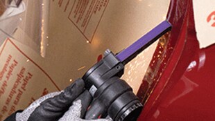 Main gantée avec outil électrique portatif et une bande abrasive étroite sur une surface métallique, produisant de petites étincelles
