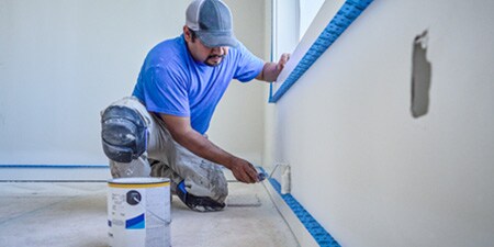 Un peintre professionnel peint un mur et utilise du ruban de masquage ScotchBlue™ PRO Finitions Parfaites pour obtenir des bords nets et précis.
