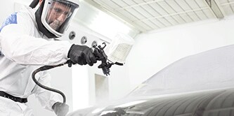 Un technicien en peinture pulvérise un véhicule
