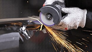 Main gantée avec meule rotative sur du métal, créant des étincelles brillantes
